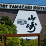 Fachada de ladrillo rojo y silueta industrial de la Destilería de Whisky Yamazaki en Japón bajo un cielo despejado.
