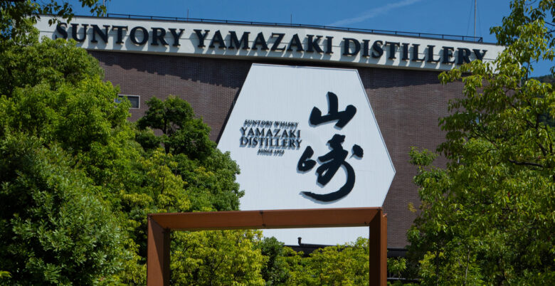 Fachada de ladrillo rojo y silueta industrial de la Destilería de Whisky Yamazaki en Japón bajo un cielo despejado.